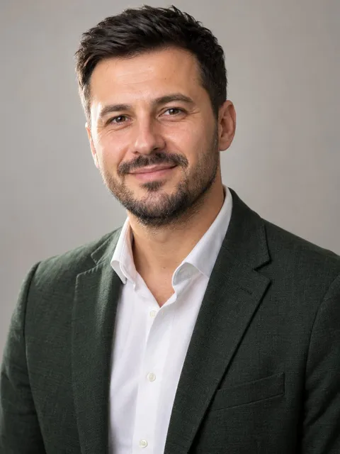 Portret al lui Andrei Moldovan, cu cămașă albă și sacou verde închis, pe fundal gri