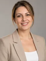 Portret al Carmenei Tudose, cu sacou bej și cercei cu perle, pe fundal gri