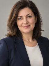 Portret al Irinei Vlădescu, cu sacou bleumarin, zâmbind, pe fundal gri